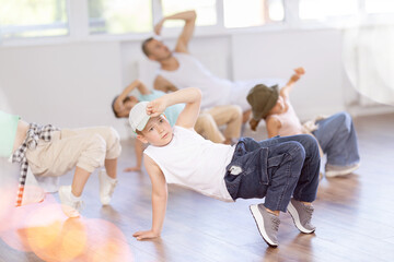Expressive cheerful teen boy practicing hip-hop movements on floor during group dance class with teacher in modern studio