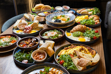 Assorted restaurant style breakfast table with eggs, pastries, salads, and fresh bread
