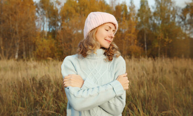 Obraz na płótnie Canvas Happy smiling woman hugs herself in autumn park enjoying warm weather on sunny day outdoors