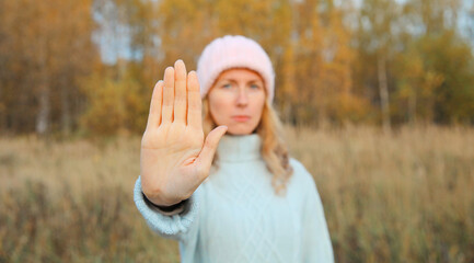 Young woman shows no, stop sign with palm of hand outdoors, refusal gesture