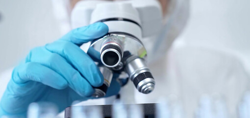 Professional scientist in protective gear is using microscope in a laboratory setting, close-up. Science and medicine concepts