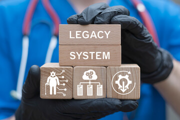 Legacy System Health Care Medicine Patients Database Obsolete Technologies Interoperability Modernization concept. Doctor holding wooden blocks with icons sees the inscription LEGACY SYSTEM.