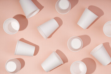 Pattern of white paper cups for drinks on pink background with hard light. Ecological disposable tableware for coffee, tea or water.