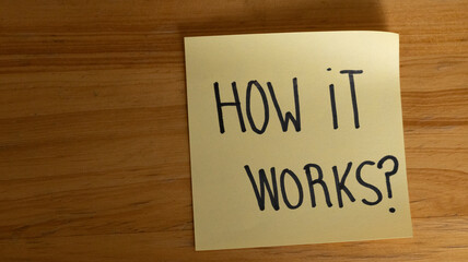 Yellow sticky note with handwritten HOW IT WORKS? on wooden surface, ideal for educational, instructional, and motivational design themes