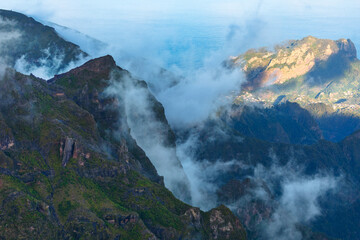 Mist weaves through rugged peaks of Pico Ruivo, Madeira, creating mystical atmosphere over dramatic mountain landscape. Shadows and sunlight highlights the island wild, natural beauty