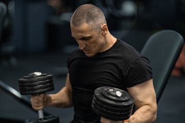 athletic man focuses intensely while lifting dumbbells on a bench in a gym setting. The environment...