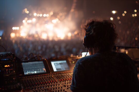 Back view of sound engineer operating audio mixer at concert with crowd, concept for live music production, event management and broadcast engineering