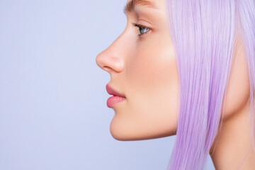 Naklejka premium Profile portrait of a woman with lavender hair in soft light, highlighting smooth skin, defined nose, and calm expression against a pale blue backdrop.
