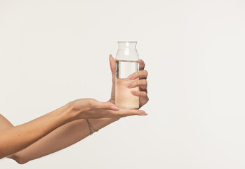 female hands holding glass transparent open bottle with water on white background