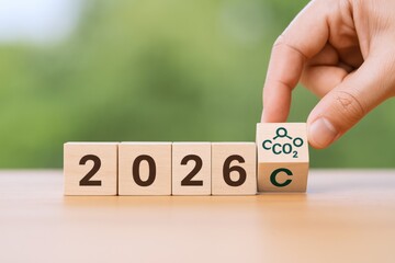 Year 2026 Carbon Reduction Strategy: Hand Placing CO2 Block on Wooden Table with Blurred Green Background