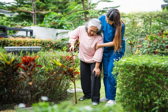 Senior care and assistance, Young caregiver helping senior woman to walk with a cane in the garden, Nurse helping an elderly patient for a walk outdoors
