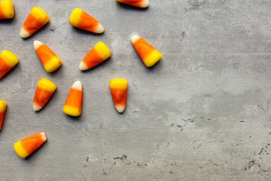 close-up of bright colored candy corns scattered against a gray backdrop with copy space available in a horizontal orientation