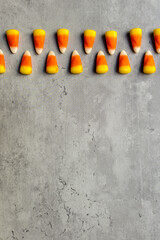 two rows of bright colored candy corns laid at the top of a gray backdrop in a vertical orientation, Halloween themed
