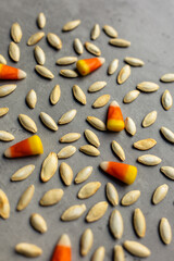 close-up of roasted pumpkin seeds and bright colored candy corn scattered against a gray backdrop in a vertical orientation