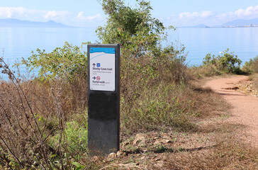 Sign for the Shelly Cove Trail and Forts Walk amongst long grass at Cape Pallarenda in Townsville, Queensland, Australia