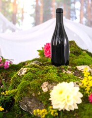 Black bottle on mossy rock surrounded by flowers