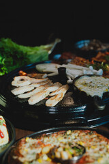 Sizzling Korean BBQ pork belly (samgyeopsal) on tabletop charcoal grill with rising smoke and traditional banchan side dishes, close-up shot in cozy restaurant setting with copy space.