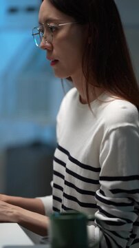 A smiling female programmer works at her computer workstation in a tech office. She is happy with her progress on a complex software development project after hours.