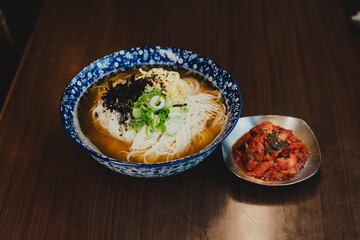 Sizzling Korean BBQ pork belly (samgyeopsal) on tabletop charcoal grill with rising smoke and traditional banchan side dishes, close-up shot in cozy restaurant setting with copy space.