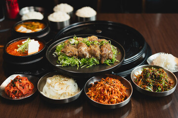Sizzling Korean BBQ pork belly (samgyeopsal) on tabletop charcoal grill with rising smoke and traditional banchan side dishes, close-up shot in cozy restaurant setting with copy space.
