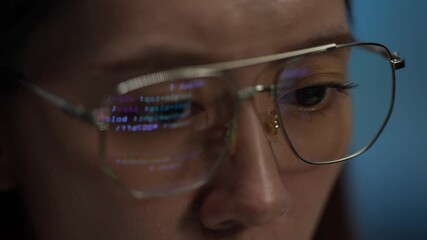 An extreme close-up of a young woman's glasses reflecting computer code. She is working late at night, focused on a complex technology problem on her screen. - Powered by Adobe