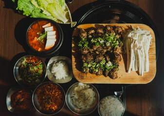 Grilled Korean beef short ribs (galbi) with caramelized edges on hot grill, served with lettuce wraps and kimchi, authentic Korean barbecue dining experience, overhead view.