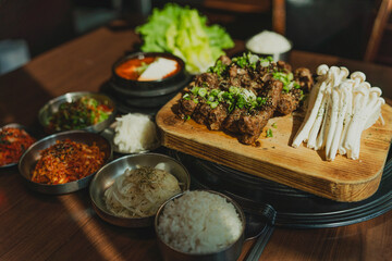 Grilled Korean beef short ribs (galbi) with caramelized edges on hot grill, served with lettuce wraps and kimchi, authentic Korean barbecue dining experience, overhead view.