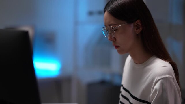 A female software developer analyzes code on her monitor. She is engaged in a deep work session, debugging a program or reviewing system architecture in a tech office at night.