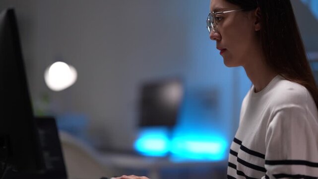 A female software developer analyzes code on her monitor. She is engaged in a deep work session, debugging a program or reviewing system architecture in a tech office at night.