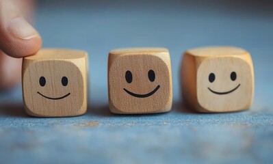 Close-up of three wooden blocks with smiling faces, one being touched by a hand, conveying happiness and positivity