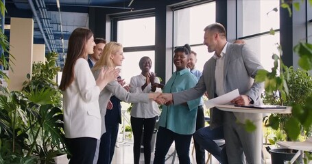 Slow motion video of young happy businessman shaking hands with a woman colleague celebrating success, making deal, business achievement with group of people applauding in modern office. 4k video.