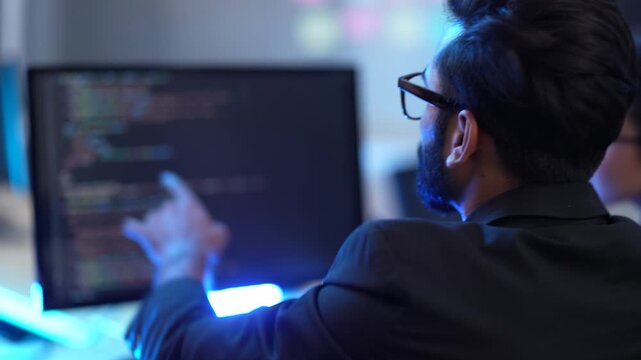 A team leader mentors his group of IT professionals in a high-tech office. They are collaborating on a complex software project, working late to meet a project deadline.