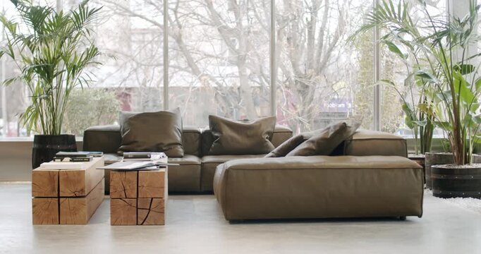 Modern living room interior with comfortable leather sofa and wooden coffee table. Large windows offer natural light, creating a cozy atmosphere. Plants and home decor complete the scene of a peaceful