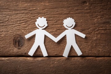 Two paper cutouts of men holding hands on a rustic wooden surface