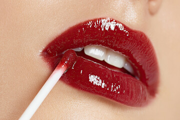 Naklejka premium A close-up of a woman's lips being applied with glossy red lip gloss, showcasing a vibrant color and smooth finish.