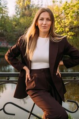 Female confidence. Outdoor portrait. Independent smiling business woman wearing suit posing in spring park at river bank.