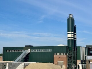 Obraz premium Large green warehouse with conveyor and sand piles in industrial area