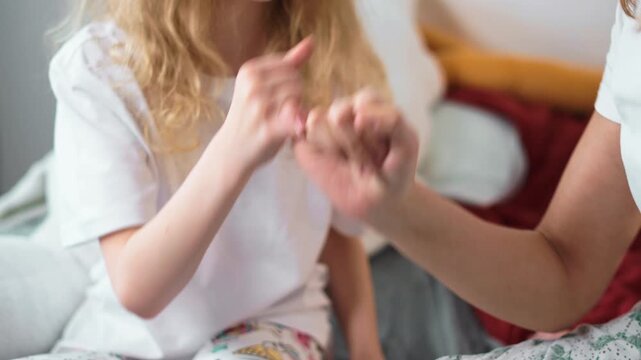 Mother and daughter making pinky promise on bed in matching pajamas. Trust, closeness, and emotional support shown in real family interaction