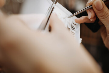 Eyelash extensions. Hand of makeup artist takes eyelashes with tweezers for subsequent gluing of extensions