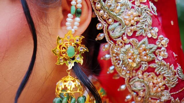 Bride ear with traditional jewelry and embroidered fabric. Golden earring decorated with green stones and pearls, along with a strand of small white pearls.
