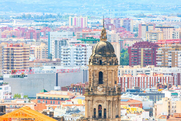 Naklejka premium Historic cathedral tower rises above colorful cityscape of Malaga, Andalusia, framed by modern apartments and distant hills. Heritage and urban growth in southern Spain