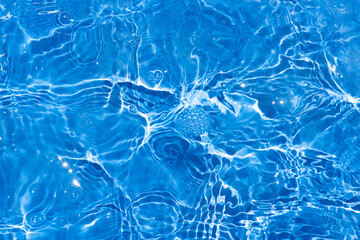 Blue water with ripples on the surface. Defocus blurred transparent blue colored clear calm water surface texture with splashes and bubbles. Water waves with shining pattern texture background.