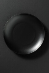 Minimalist black ceramic plate, placed on a dark textured background