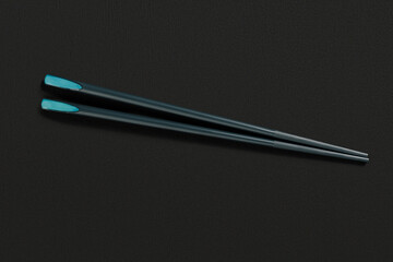 Chopsticks in dark material, placed on a black textured background