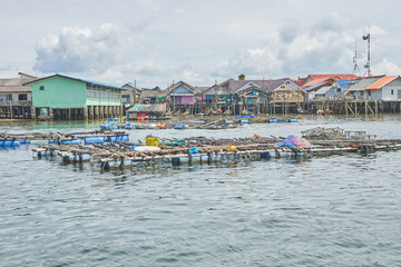 PHUKET, THAILAND - 12 NOVEMBER 2017: Coastal fishing village with stilt houses and floating fish farms in tranquil waters under cloudy sky.