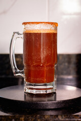 Refreshing and spicy michelada cocktail is garnished with a chili powder rim and sits on a black coaster