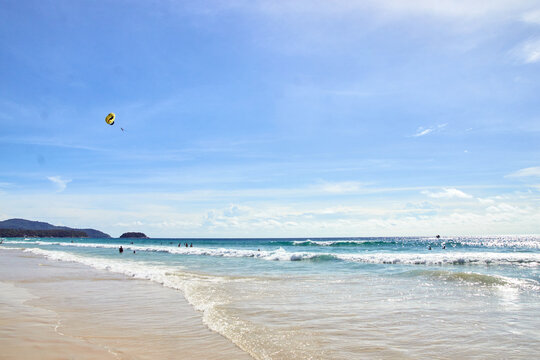 PHUKET, THAILAND - 13 NOVEMBER 2017: Sunny beach with clear blue skies and waves as people enjoy parasailing in the distance.