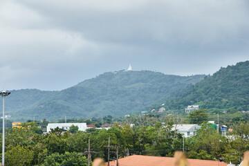 PHUKET, THAILAND - 2 NOVEMBER 2017: Scenic view of lush green hills with distant white statue under cloudy sky.