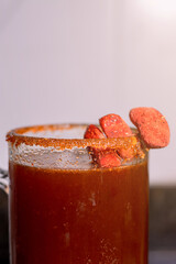 Glass of a traditional mexican michelada cocktail, featuring a chili-lime salted rim and garnished with dried chili peppers