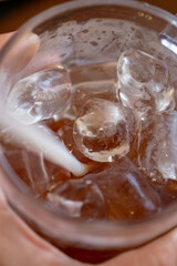  Extreme close-up of a glass mug's interior, showing large, clear ice cubes and a white plastic straw in a dark brown iced tea. A hand is blurred in the background holding the glass.